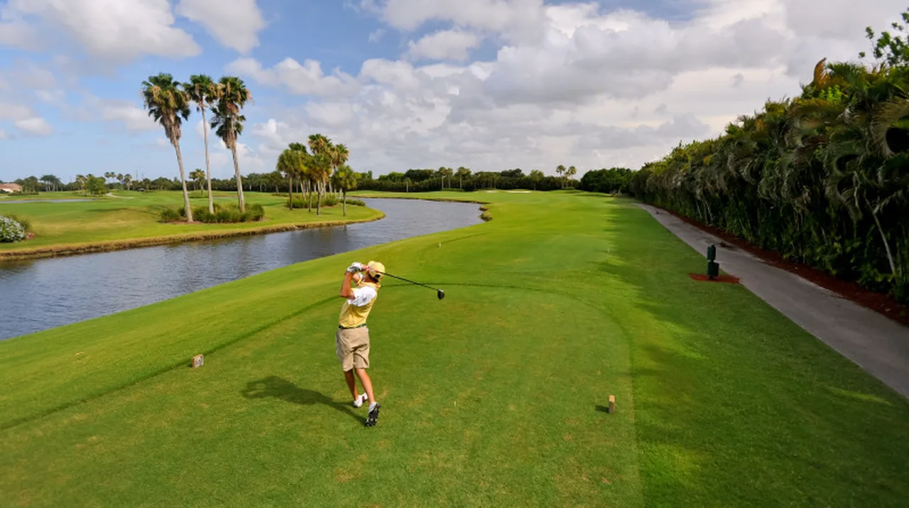 A golfer teeing off at the North Palm Beach Country Club in North Palm Beach, Florida, water and palms along the fairway