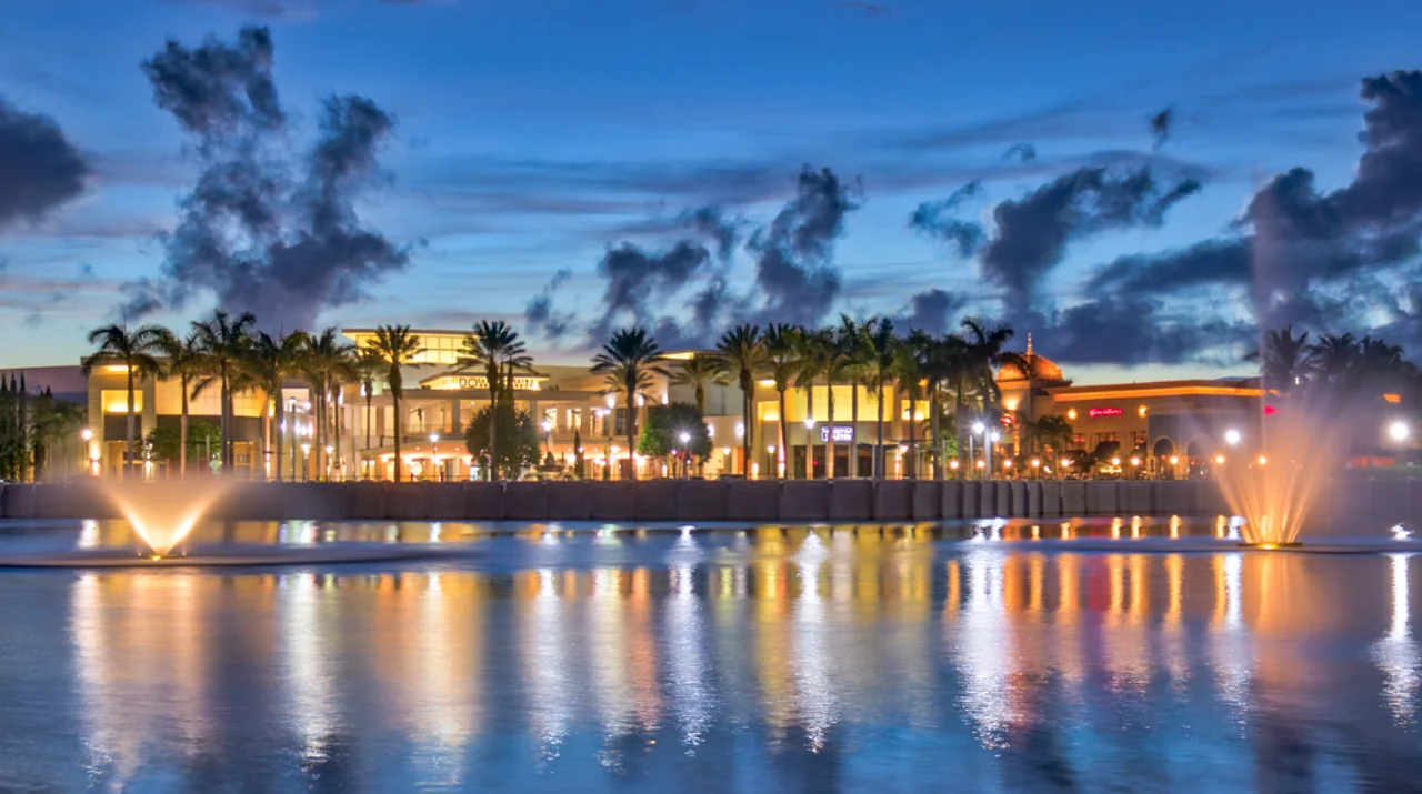 Downtown Palm Beach Gardens, Florida at dusk, fountains on the lake in front of the lit shops and restaurants